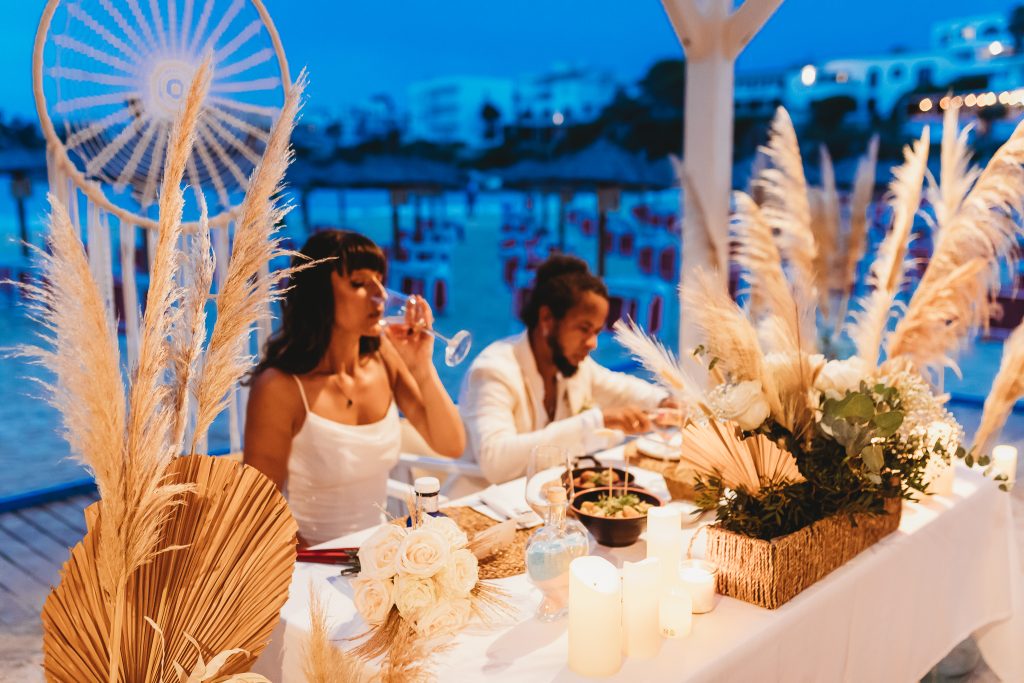 Romantic seaside wedding dinner at dusk with pampas grass décor, candlelight and a couple enjoying an intimate reception by the water in Mallorca.