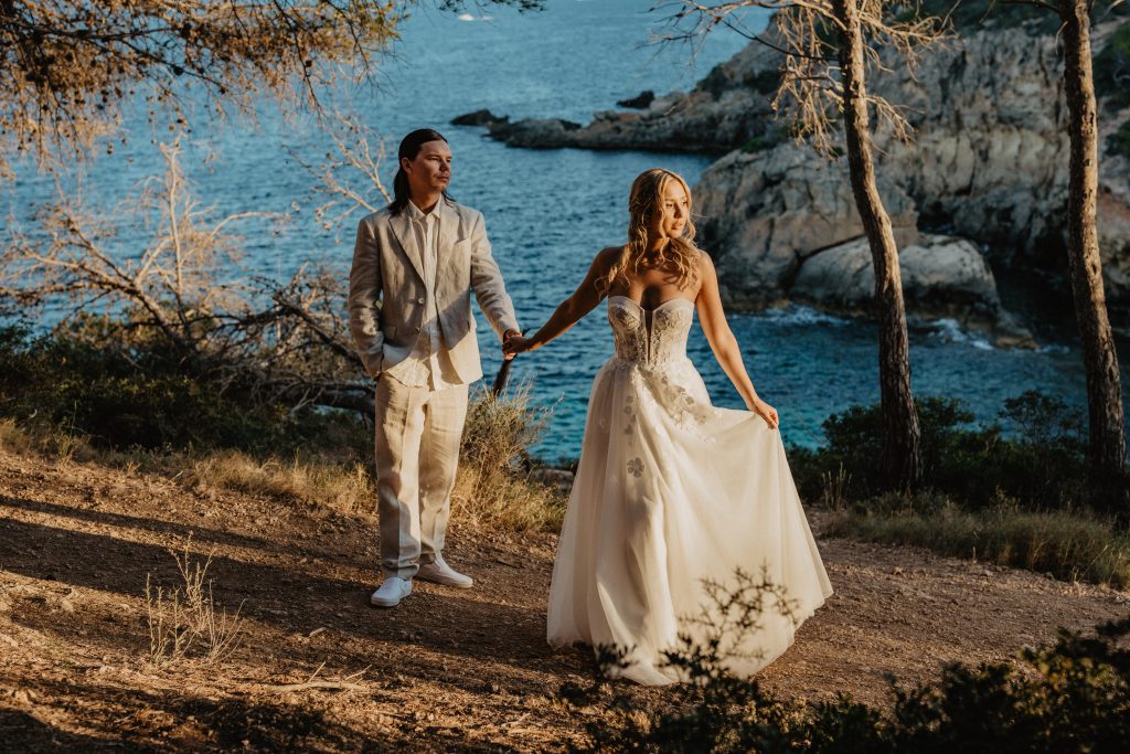 Bride and groom walking hand in hand along the Mallorca coastline during an intimate destination wedding photoshoot.
