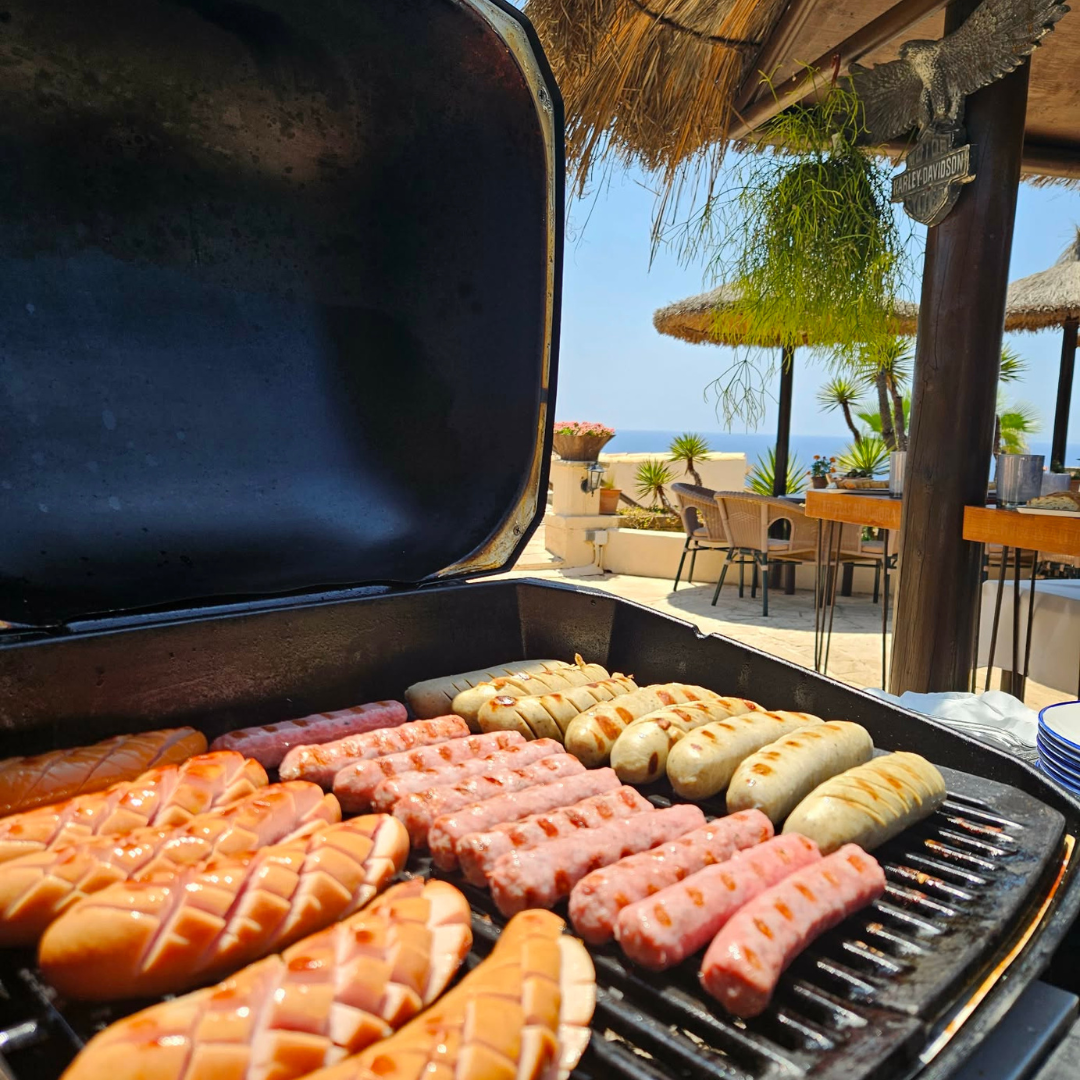 Grilled sausages and hot dogs prepared on an outdoor barbecue as part of wedding catering by the sea.