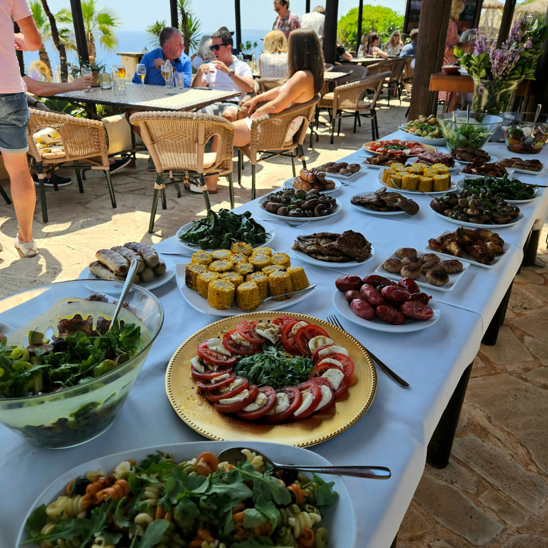 Outdoor wedding buffet with a variety of salads, grilled dishes and appetizers served on a long table.