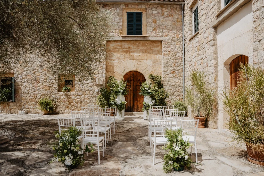 Outdoor wedding ceremony space at a historic Mallorcan stone finca — white chairs, floral arrangements and ancient stone architecture in natural daylight